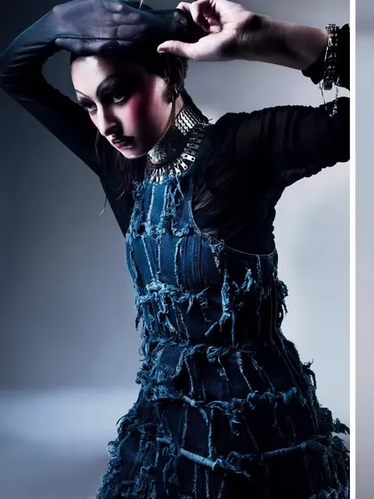 A dynamic pose from the same editorial, showing the model adjusting her headpiece. The lighting highlights the texture of the dress and the metallic sheen of the necklace.
