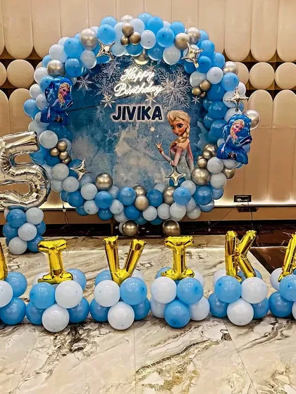A magical Frozen theme for a 5th birthday. This setup features a circular backdrop with Elsa, a large silver foil '5', and balloon lettering for the name, all in an icy blue and silver color scheme.