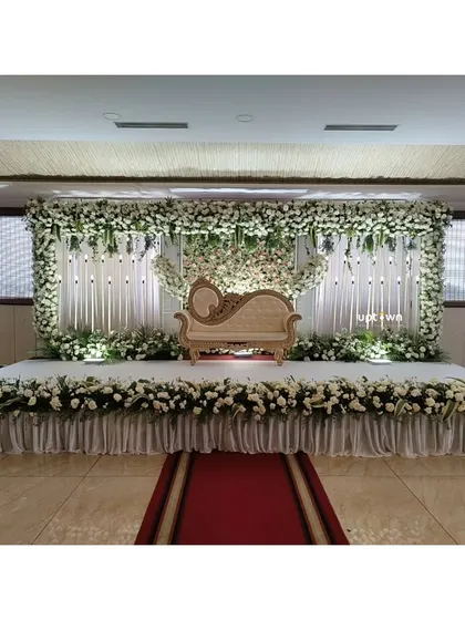 We design elegant stages for engagements and receptions that feel both grand and personal. This setup features a full floral frame of white rose's and lush green's, a classic diwan for the couple, and professional stage lighting to create a beautiful focal point for the event.