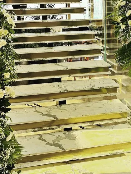 A floral arch adorns a marble staircase, combining classic white roses with fresh greenery to create an elegant and timeless decorative element within the venue.