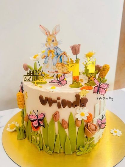 A charming Peter Rabbit themed cake. The design includes buttercream grass and flowers, creating a lovely garden scene right out of the storybook.