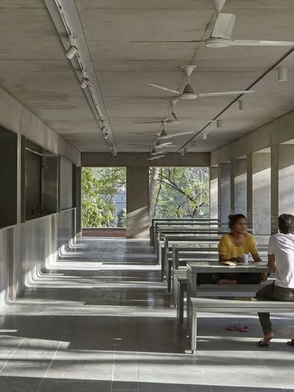 The interior of the CEPT University Canteen features long communal tables and benches made of simple, durable materials. The design creates a functional and robust space for dining and socializing, with natural light filtering in from the open sides.