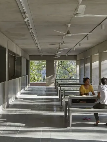 The interior of the CEPT University Canteen features long communal tables and benches made of simple, durable materials. The design creates a functional and robust space for dining and socializing, with natural light filtering in from the open sides.