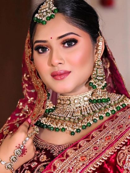 A bride in a maroon velvet lehenga wearing a matching Kundan set with green beads. The hand jewellery, or hathphool, adds an extra layer of elegance.