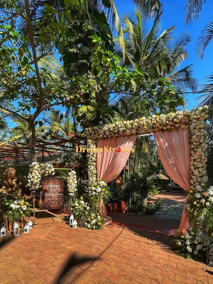 A grand floral archway with soft peach drapes creates a stunning entrance for a summer wedding, blending perfectly with the surrounding greenery.