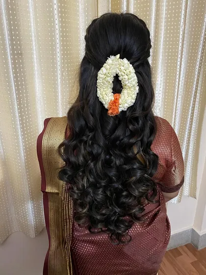 This half-updo features soft, bouncy curls and is adorned with a fresh jasmine gajra. It's a beautiful fusion of modern and traditional styles for any pre-wedding event.