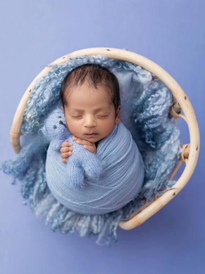 A wider, top down view of the baby boy and his teddy bear, nestled in a round wicker prop. The shades of blue create a calming and serene atmosphere.