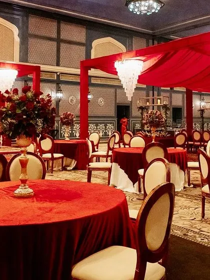 Guest dining tables set for a royal wedding, with red velvet tablecloths and elegant cream-colored chairs creating a rich and inviting look.