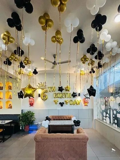 A full room decoration for a 6th birthday party in a cafe. The ceiling is covered with black, gold, and white balloons, creating a festive and immersive party environment.