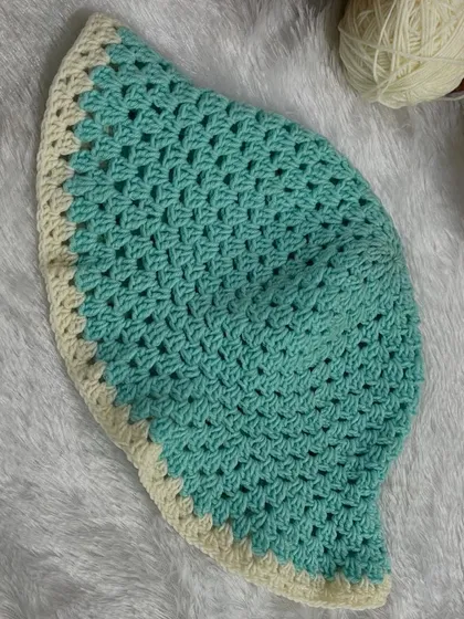 A flat-lay of the sea green and cream crochet bucket hat. This view shows the classic circular construction and the detailed stitch work.