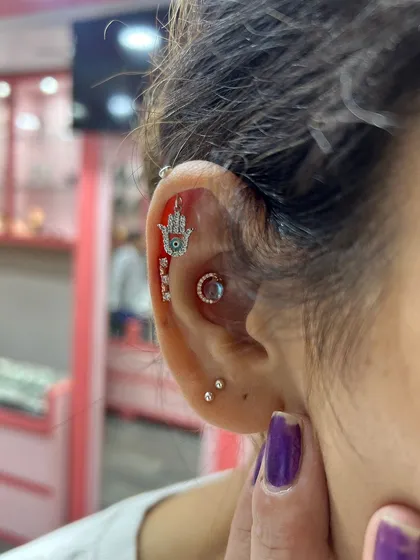 A protective and stylish Hamsa hand hanging from the helix, paired with a ruby conch stud and other delicate pieces.