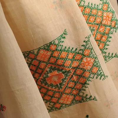 Another beautiful memory, this fabric shows intricate phulkari-style embroidery with bright orange and green threads on a light cotton base.