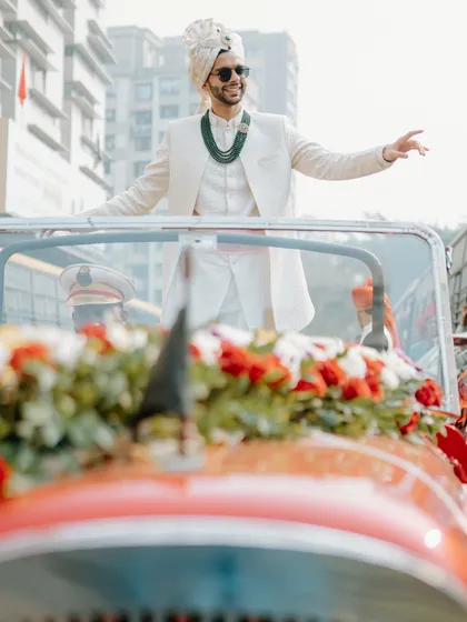 The groom arriving in style in a vintage red car. We arrange for unique transportation to make the baraat procession truly memorable.