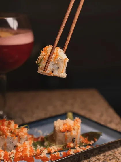 A close-up shot that puts you right at the table. Using chopsticks to lift a piece of sushi creates a sense of interaction and highlights the delicate textures and toppings of the dish.