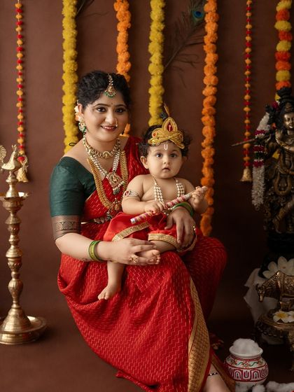 A formal portrait of a mother and her son in a detailed Krishna costume, complete with a flute and crown.