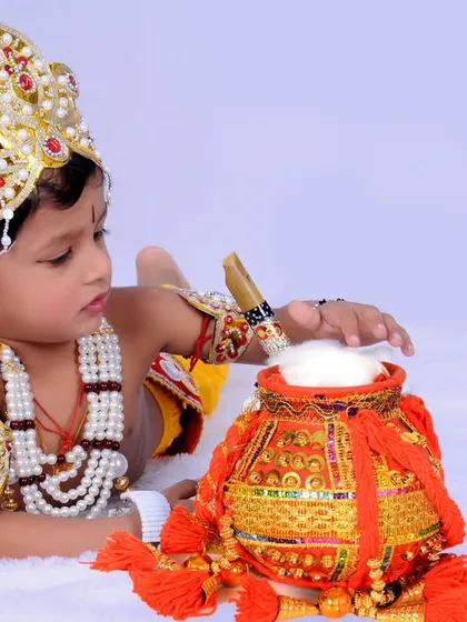 A classic pose of a young child as Krishna, reaching for the pot of butter. I use a clean white background to make the colorful costume and props stand out.