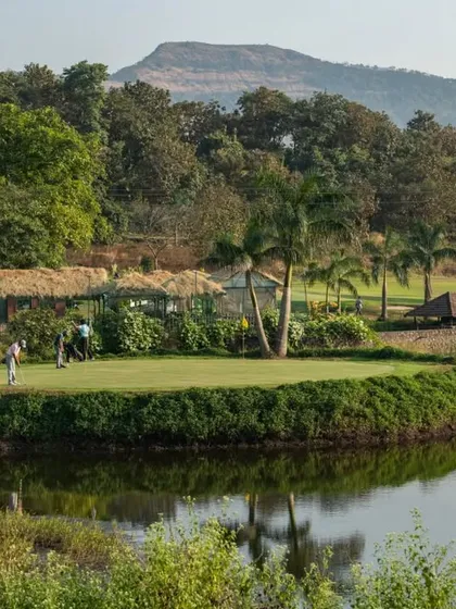 A picturesque view across the water to one of our greens, where players are enjoying a round. The reflection in the water and the thatched-roof huts create a tranquil, resort-like atmosphere.
