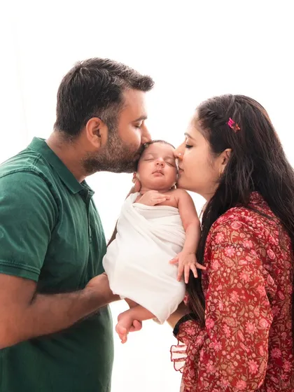 Sealed with a kiss. Both parents gently kiss their newborn's head in this classic, minimalist portrait that beautifully isolates a moment of pure family love.