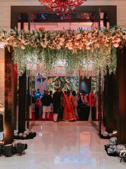 The grand entrance to the Sangeet, adorned with a lush floral canopy and hanging greenery, creating a warm and inviting welcome for guests.