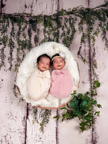 Two little bosses sleeping peacefully in a hanging basket adorned with greenery. This setup creates a dreamy, ethereal feel for a twin newborn session.