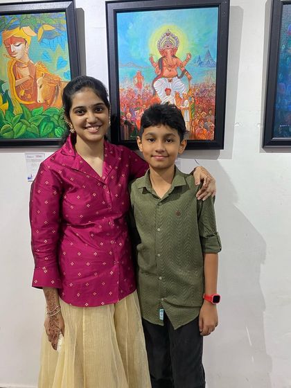 An artist posing with a young student in front of her exhibited paintings.