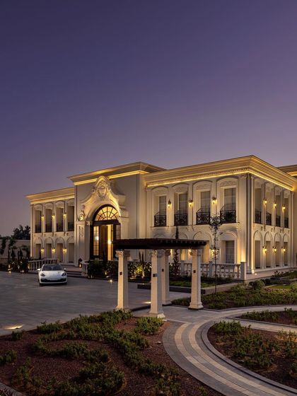 A twilight view of The Grand Alabaster, showcasing its impressive scale and beautifully landscaped driveway. The warm interior light spilling from the windows creates an inviting contrast with the regal exterior.