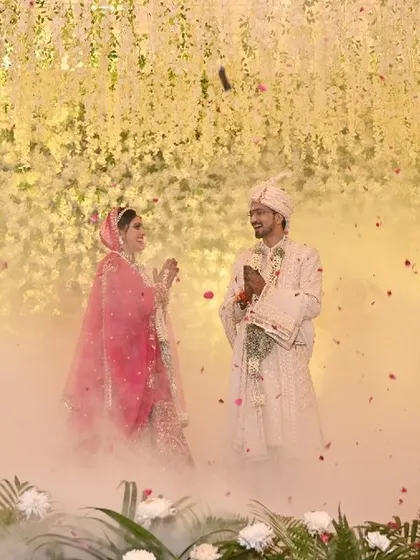 An intimate moment during the Jaimala, with the couple smiling at each other amidst a cloud of smoke. Dancers with props stand like statues, framing this beautiful exchange.