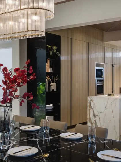 This view shows the seamless connection between the dining area and the kitchen in our Celadon project. The black marble dining table and statement chandelier provide a touch of formal elegance, while the marble kitchen island and light wood cabinetry maintain an open, inviting atmosphere for family gatherings.