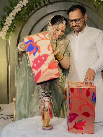 The pure joy of the reveal. This mom-to-be is all smiles as she lifts the lid of the custom Paithani-print box to reveal the doll inside.