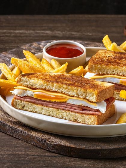A breakfast sandwich with ham, egg, and cheese, served with fries and ketchup.