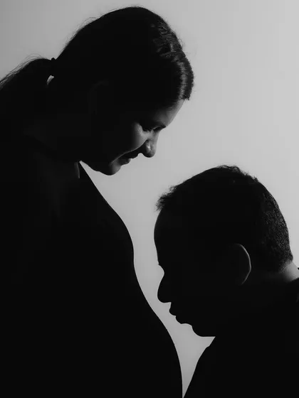 This artistic silhouette focuses on the profound connection between the father-to-be and his unborn child. The dramatic lighting strips away all distractions, leaving only the pure, emotional bond in this powerful black and white maternity photograph.