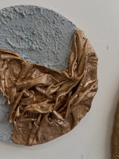 A close-up of a set of circular artworks made for a client in Dubai. This series combines a rough, grey, concrete-like texture with shimmering, sculpted gold fabric.