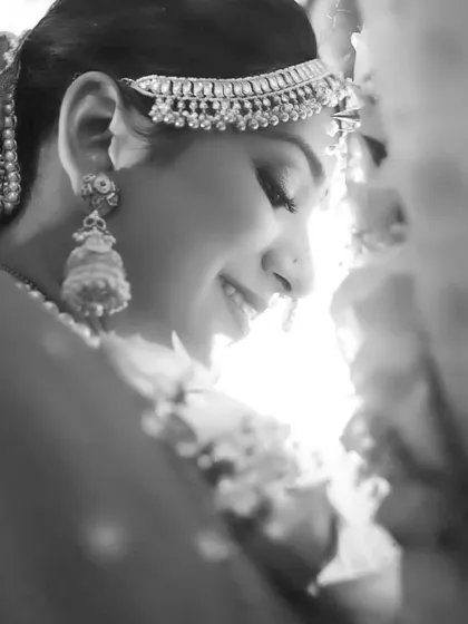 A close-up black and white portrait of the bride, blushing. The high-key lighting creates a soft, angelic glow.