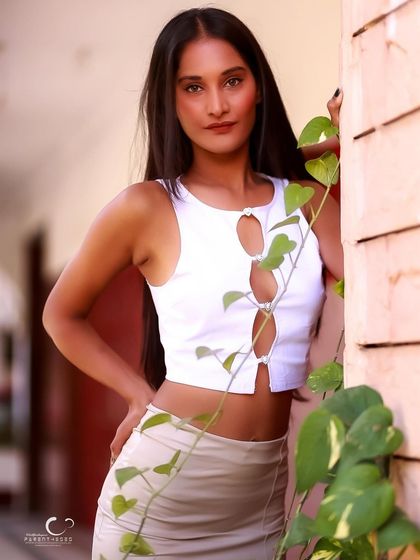 A chic and modern outdoor portrait. The simple white top and beige skirt look fresh and stylish against the natural backdrop of a money plant.