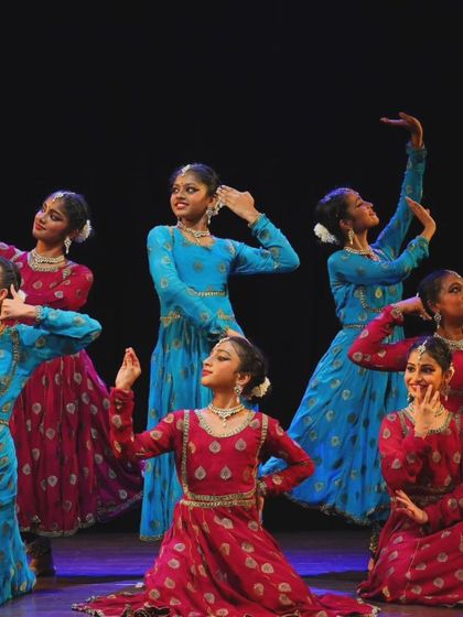 My students from the Sāttvatī School of Dance in a dynamic pose during our "ARAMBH" performance, dressed in vibrant red and blue costumes.