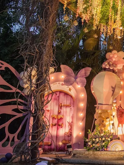 The entrance to Hitanshi's enchanted garden, featuring a large pink door prop with butterfly details, set against a natural, rustic backdrop.