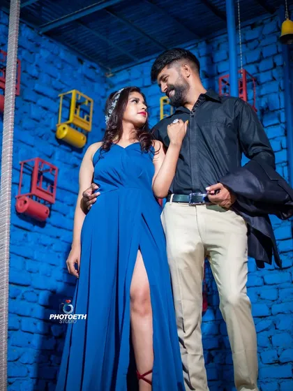A modern and stylish pre-wedding portrait against a textured, bright blue wall. The couple's confident pose and coordinated outfits create a strong, fashionable look.