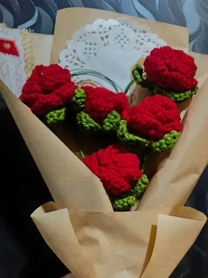 A close-up of the five red crochet roses. You can see the detail in each petal and the lush green leaves that accompany them.