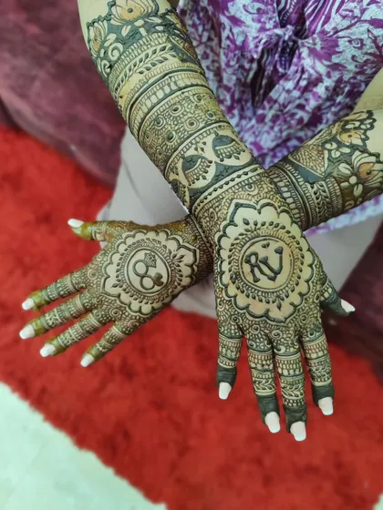 An engagement mehendi with the couple's initials inside a beautiful mandala. The arms are decorated with traditional bands and peacock motifs.