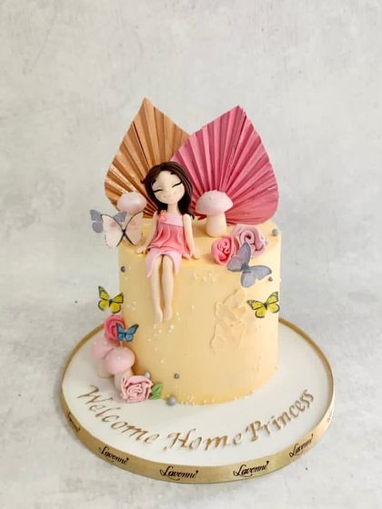A sweet "Welcome Home Princess" cake. The design features a sitting princess figurine, butterflies, and delicate sugar flowers.