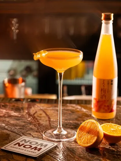 A bright orange cocktail in a coupe glass, shot on a marble bar top. The focus is on the color and the elegant glassware.