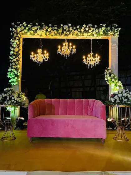 A simple yet chic seating area for a reception or sangeet. The pink sofa adds a pop of color, while the chandeliers and floral arrangements create an elegant and inviting atmosphere.