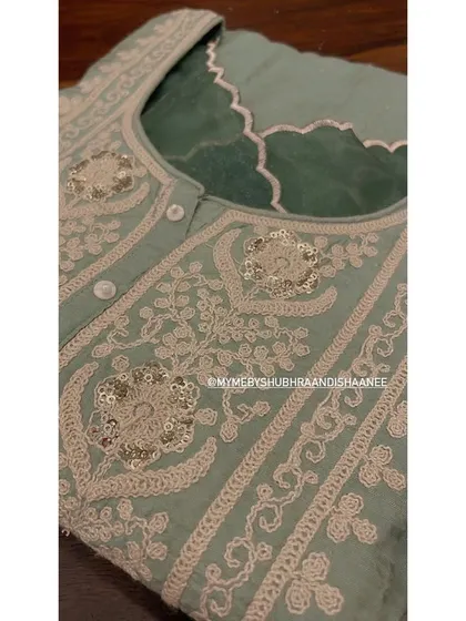 A close-up of the exquisite embroidery on a sage green kurta. The intricate threadwork is complemented by carefully placed sequins, adding a subtle shimmer to the piece.