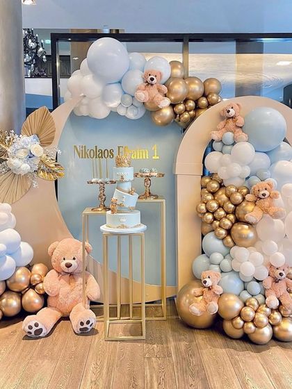 An elegant teddy bear theme using a soft blue, white, and gold color palette. The setup features modern arched backdrops and organic balloon clouds for a sophisticated look.
