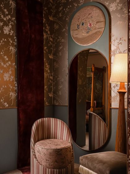 Welcome to Zone Two, a space inspired by the softness and intricacy of a boudoir. Here, a custom mirror with an embroidered panel sits beside a striped chair and a unique wall rug that appears to spill onto the floor, creating a sense of movement.