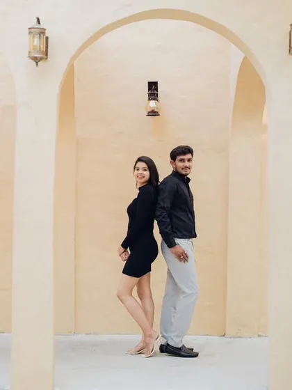 A playful, back-to-back pose in a minimalist studio setting. This shot shows the couple's fun side while maintaining a chic, fashionable aesthetic with their coordinated modern outfits.