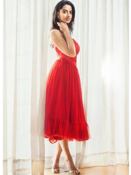 A side profile of the red tulle gown, highlighting its delicate layers and romantic silhouette. The styling is soft and elegant, focusing on form and texture.