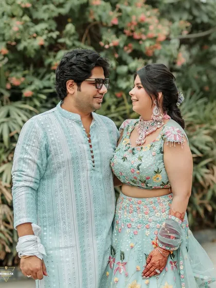 A sweet couple portrait from the Haldi event, their coordinated pastel outfits looking beautiful against the natural green backdrop.