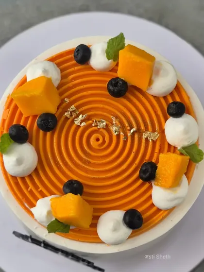An overhead view of the fresh Alphonso mango cake, showing the precise spiral design and the placement of fruit and edible gold leaf.