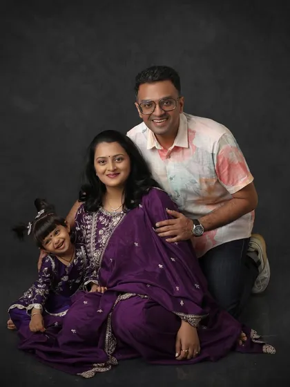 A beautiful family story. This maternity portrait includes the couple's older daughter, all dressed in matching purple outfits, celebrating the upcoming arrival of a new family member.